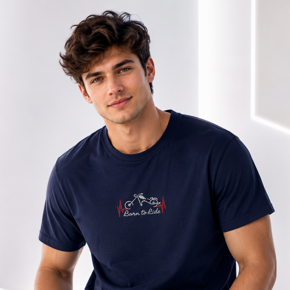 Man wearing a navy blue t-shirt with a logo and text, sitting against a white wall.