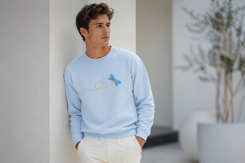 Man wearing a light blue sweater with a small design, standing indoors.
